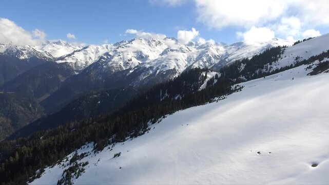 Aerial panorama shows pristine Pyrenees snow slopes, jagged summits, forest valley below. Untouched white ridgelines cover highland basin near Spain France border, quiet alpine winter scene.