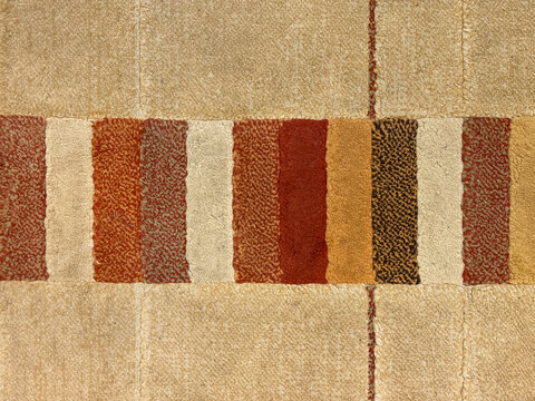 Close up of beige carpet with colorful stripes pattern in red, yellow, brown, and white color tuft. Suitable for drapery, and rug. Seamless background texture