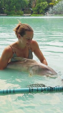 Vertical video. Woman Holding Large Pangasius Catfish In Shallow Lake Water Near Landing Net With Calm Expression, Careful Fish Handling And Catch And Release Preparation