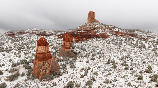 Aerial view of snow-covered red rock buttes and sandstone formations rising from a desert landscape under an overcast sky in Page, Arizona, United States.