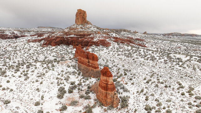 Aerial view of red sandstone buttes and rock formations covered in a light layer of snow under an overcast sky in Page, Arizona, United States.