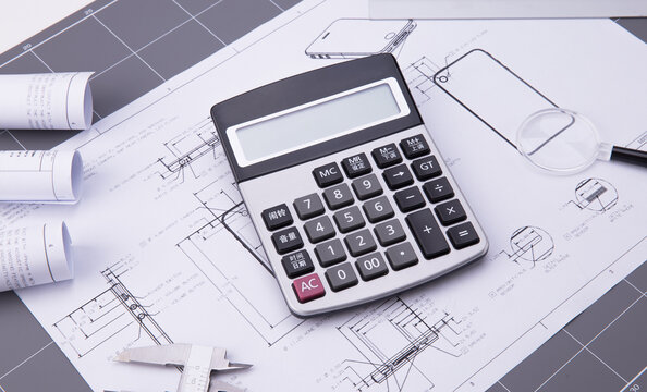 Calculator on architectural plans with measuring tools for construction budgeting