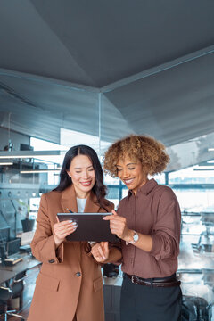 Professional business people working. Asian businesswoman, African American employee woman discussing project in office. Team leader explain trainee working process using tablet pc computer. Vertical