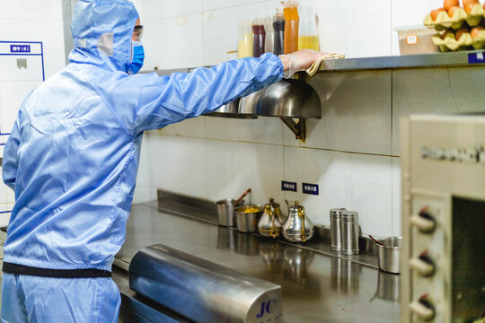 Protective worker disinfecting restaurant kitchen counter for safe reopening