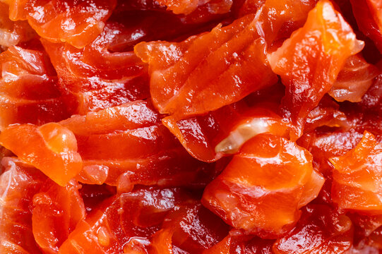A high-angle, close-up macro shot of fresh, glossy salmon sashimi pieces or salmon tartare with a vibrant orange-red texture and natural fat marbling.