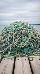 Fototapeta premium Tangled fishing nets and ropes piled on a wooden pier, conveying maritime tradition and texture in soft overcast light with copy space