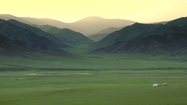 Mongolian ger tent at sunrise on treeless steppe plain, warm glow over distant hills. Traditional yurt during dawn across open grassland, soft sunbeams wash mountain ridges.