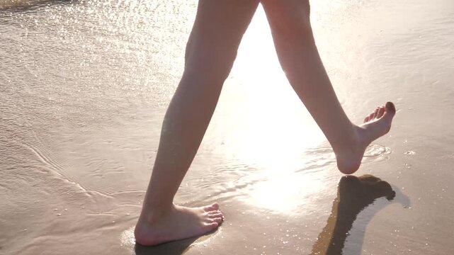 Barefoot teenager girl walking along shallow waterline on sandy beach French Atlantic