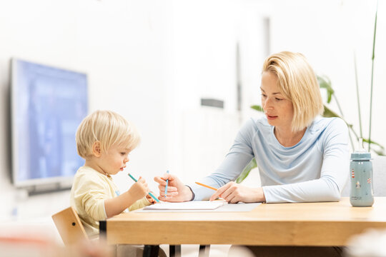 Caring young Caucasian mother and small son drawing painting in notebook at home together. Loving mom or nanny having fun learning and playing with her little 1,5 year old infant baby boy child