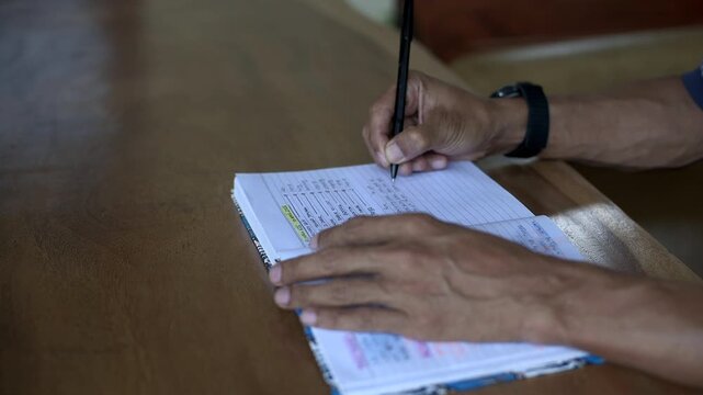 Asian male hand writing close up tripod shot on wooden table at home indicating a busy daily activity