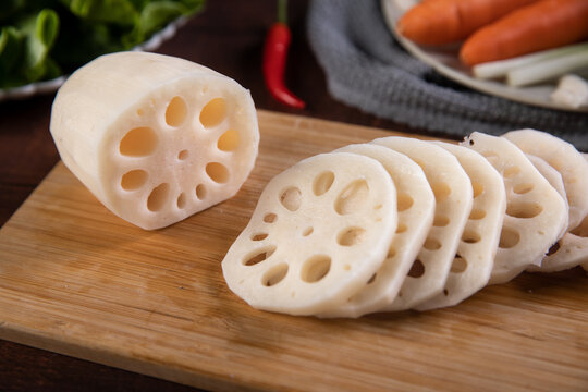 Fresh sliced lotus root on wooden cutting board with vegetables