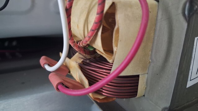Electrical transformer component showing copper wire coils and insulated red wires inside a metal device