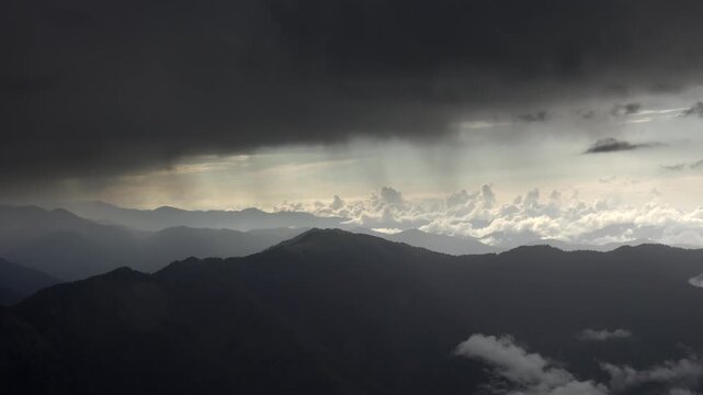 Rain timelapse over Pyrenees mountains as storm clouds sweep across layered ridgelines. Moody downpour sequence showing misty highlands, thunderheads, and crepuscular rays on summits.