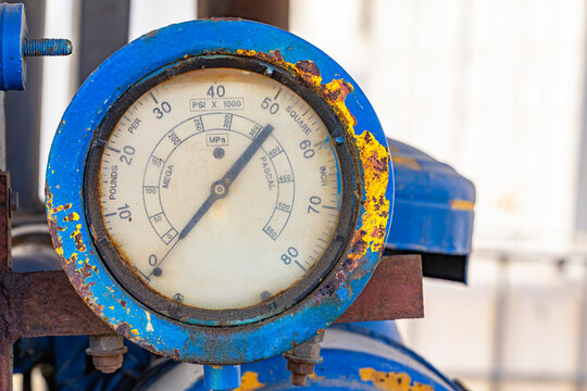 Close up of a large analog high pressure gauge on weathered blue industrial machinery with rusty metal frame