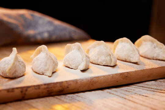 Row of raw handmade dumplings on wooden board