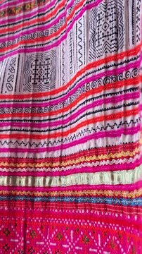  Close-up of an ancient embroidered textile with intricate ethnic patterns in vivid pink, red, and multicolor threads, showing fine craftsmanship, rich heritage, and textured folds in traditional fa