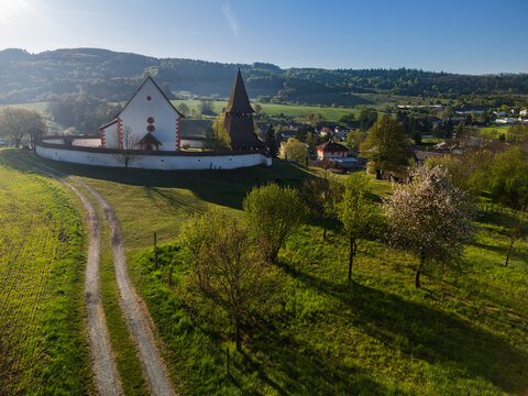 Aerial view of the historic Church of St. Martin with its wooden bell tower and fortified wall on a green hill in Cerin, Banskobystricky kraj, Slovakia.