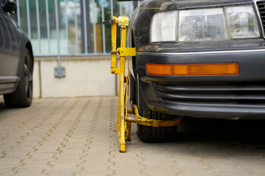 Heavy-duty yellow wheel clamp attached to the front tire of a black car.