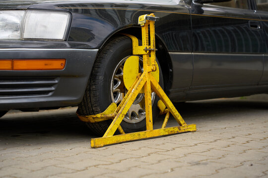 Heavy-duty yellow wheel lock on a black car tire on a city street.
