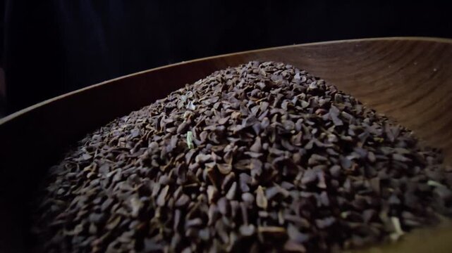 Close-up of dried Syrian Rue seeds (Peganum harmala) in a rustic wooden bowl, dark background, cinematic lighting, organic herbal texture.