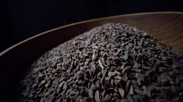 Close-up of dried Syrian Rue seeds (Peganum harmala) in a rustic wooden bowl, dark background, cinematic lighting, organic herbal texture.