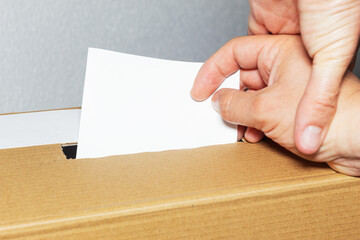 Obraz premium A hand forcing another hand to insert a ballot into a cardboard ballot box. Vote tampering, a form of fraudulent interference in the electoral process