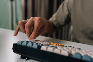Fototapeta premium Close-up of hand cleaning mechanical wireless keyboard with cotton swab, performing routine maintenance and hygiene for computer peripherals and digital devices. Concept of desktop PC maintenance.