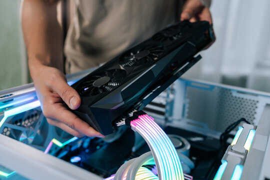 Person upgrading gaming computer, installing powerful graphics card into open pc case, showing internal components with rgb led lighting and custom liquid cooling system, close-up.