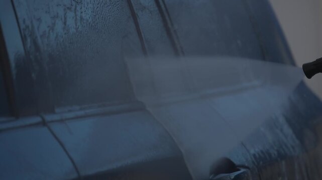 A high-pressure washer washes dark car windows with running water. Car wash concept.
