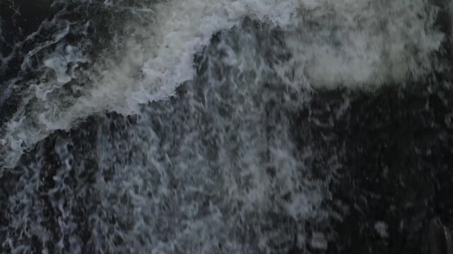 Top view of powerful water stream with white foam and splashes. Abstract texture of rushing river water at the dam