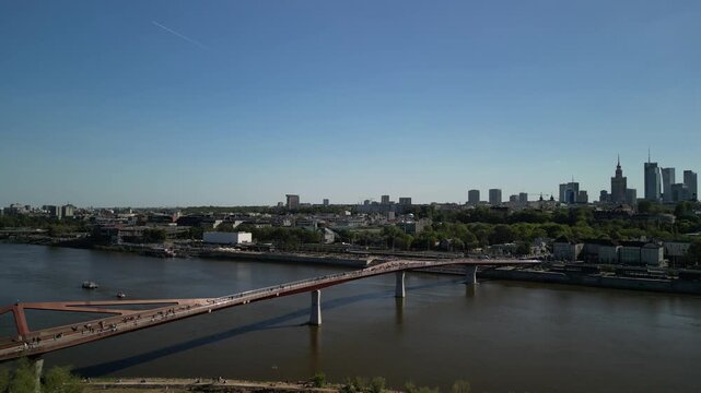 Warszawa - Polska - panorama miasta i kładka pieszo rowerowana na rzece Wisła nagrane dronem. Słońce, panorama miasta, drapacze chmur, krajobraz miasta z drona