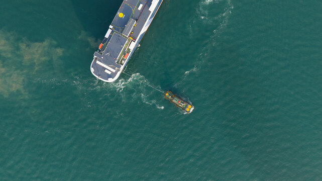 Aerial view of a large cargo ship being assisted by a tugboat in the turquoise waters of the port area in Laem Chabang, Chon Buri, Thailand.