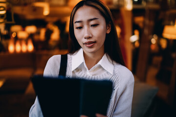 Fototapeta premium Asian woman focused on tablet screen outdoors. Captures immersive attention, remote productivity, and confidence with mobile tech in realistic freelance setting.