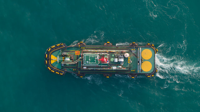Aerial view of a tugboat navigating through turquoise waters with a white wake near the port of Laem Chabang, Chon Buri, Thailand.