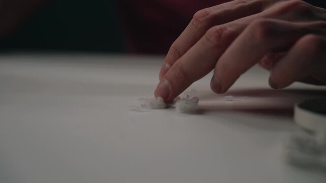 Close-up view of male hand collecting pile of white lint, fluff, pills from surface after using fabric shaver to remove them from garment for clothing care. Shooting in slow motion.