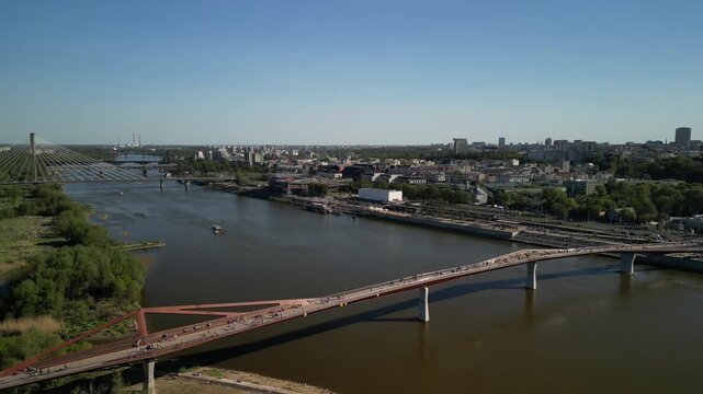 Warszawa - Polska - panorama miasta i kładka pieszo rowerowana na rzece Wisła nagrane dronem. Słońce, panorama miasta, drapacze chmur, krajobraz miasta z drona