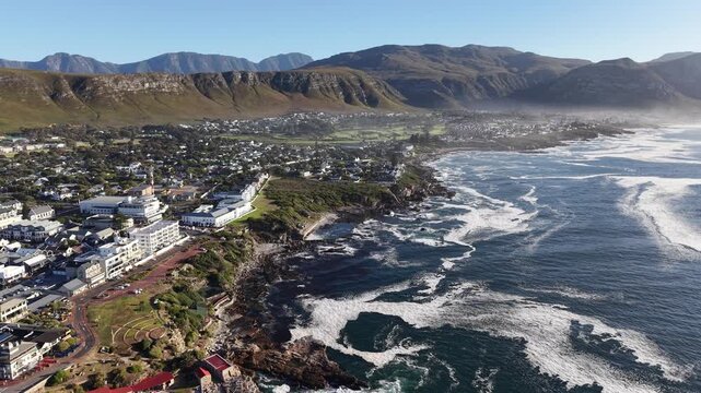 Hermanus, South Africa - January 19, 2026: Aerial drone view of Hermanus from the ocean, waves rolling along the coastline, clear blue sky and scenic seaside town in South Africa.