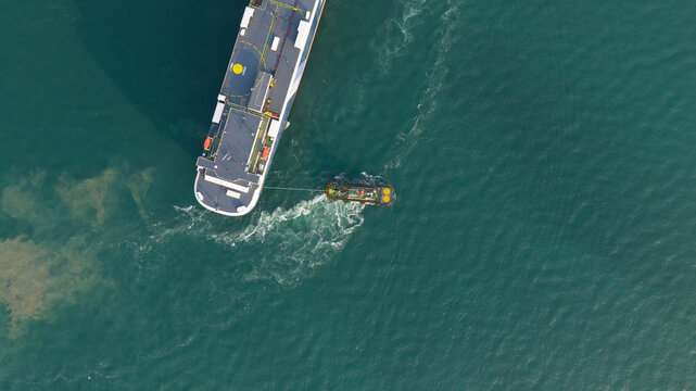Aerial view of a large cargo ship being assisted by a tugboat in turquoise waters near the port of Laem Chabang, Chon Buri, Thailand.