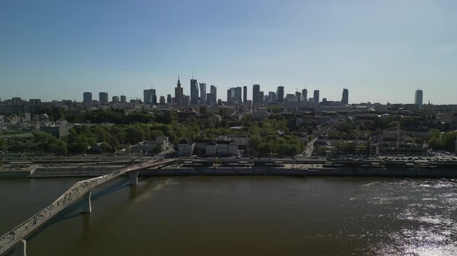 Warszawa - Polska - panorama miasta i kładka pieszo rowerowana na rzece Wisła nagrane dronem. Słońce, panorama miasta, drapacze chmur, krajobraz miasta z drona