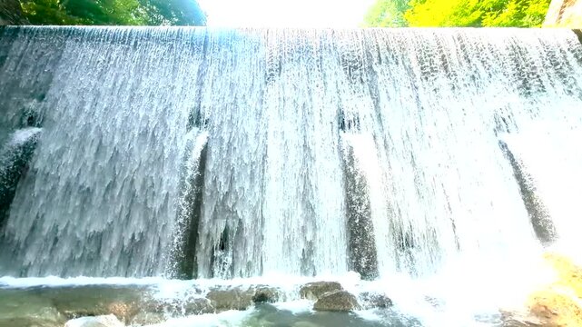 福島県南会津町の堰堤、初夏の緑に囲まれて正面から迫力ある水流が流れ落ちる水辺風景