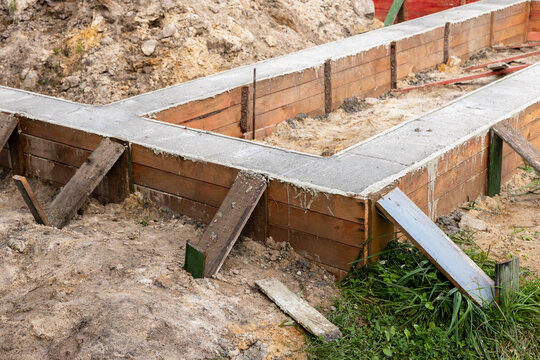Concrete foundation forms and wooden formwork on a construction site showing freshly poured footings, earthwork and temporary braces. Image conveys building progress and site preparation