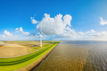 Naklejka premium Aerial view of wind turbines on green fields near sea coast and dam. Scenic landscape with wind generators, field and sky with clouds. Renewable energy and environment from above.