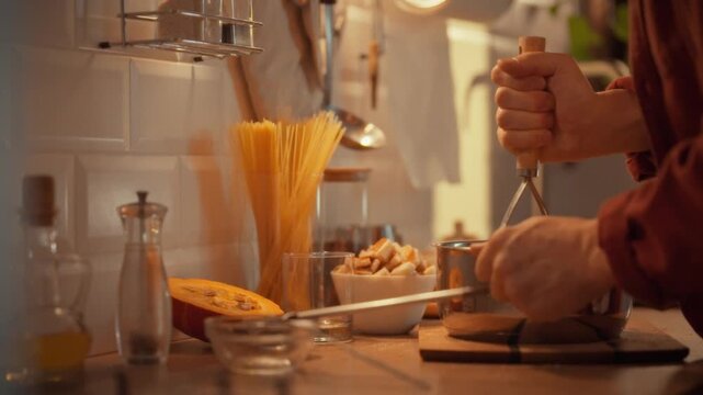 A man skillfully handles a potato masher, removing it from storage as he prepares to mash cooked potatoes in a metallic saucepan, creating a smooth vegetable puree through a simple cooking process