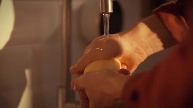 A man's hands gently rinse peeled potatoes under cool running water in a cozy kitchen, a key step in preparing fresh vegetables for cooking, highlighting his careful food-prep routine