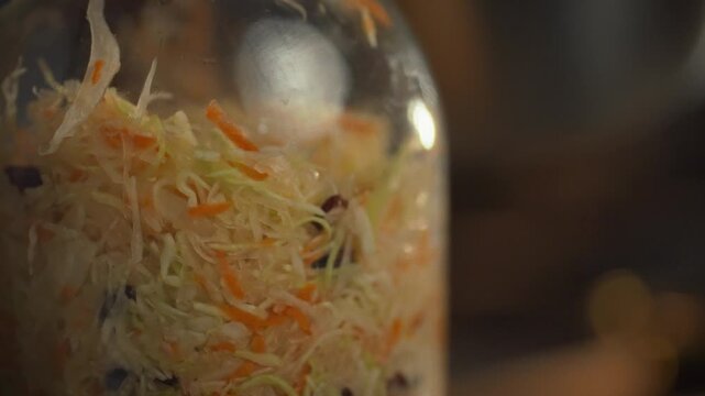 A hand spoons shredded cabbage into a jar, blending crunchy textures, ahead of fermentation, in a traditional eating culture, showcasing the tamper and utensils like bowls