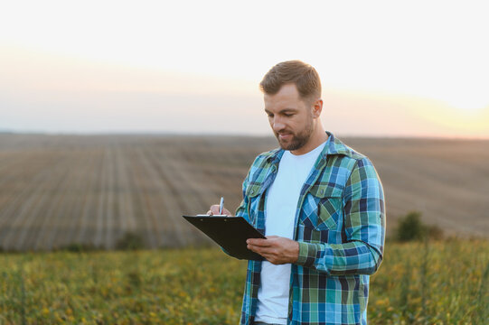 Farmer writing notes on clipboard in soybean field at sunset