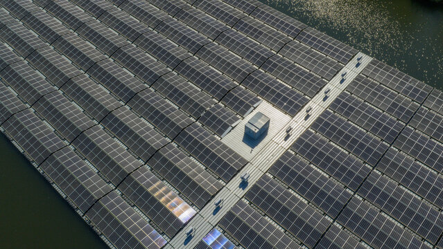 Aerial view of a large floating solar farm with rows of photovoltaic panels reflecting sunlight on a calm body of water in Zwolle, Overijssel, Netherlands.