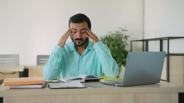 Stressed Indian man suffering from headache at work