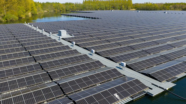 Aerial view of a large floating solar farm with rows of photovoltaic panels on a calm lake surrounded by green trees in Zwolle, Overijssel, Netherlands.