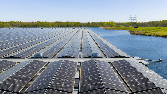 Aerial view of floating solar panels on a calm lake surrounded by lush green forests and power lines under a clear sky Zwolle, Overijssel, Netherlands.